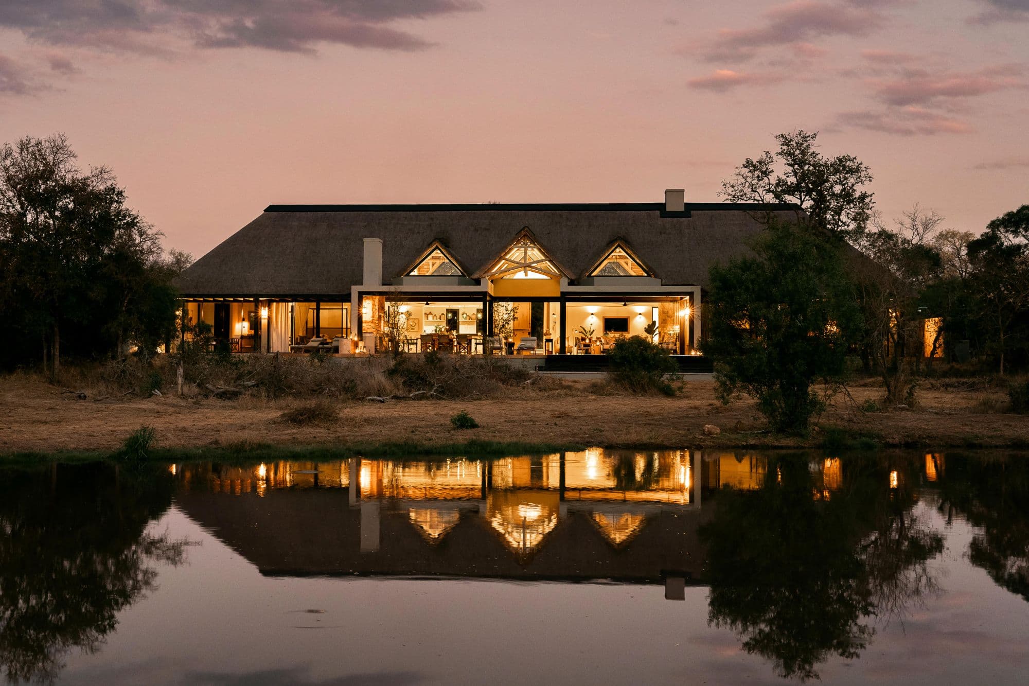 Monwana Game Lodge at dusk, lit gables reflected in the waterhole